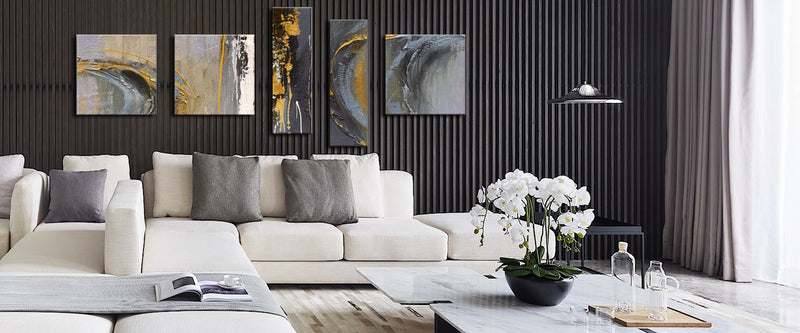 Een moderne woonkamer met een beige hoekbank, abstracte kunstwerken boven de bank, marmeren salontafel met orchideeën en glazen set, en een strakke hanglamp.