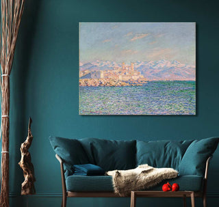 Claude Monet's Het kasteel van Antibes oil painting in impressionist style, elegantly displayed above a teal loveseat in a cozy interior setting.