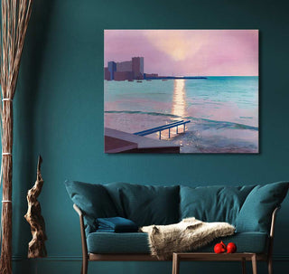 David Hockney's Early Morning in Sainte Maxime painting, depicting a pastel seascape at sunset with a silhouetted shoreline, hangs above a teal loveseat.