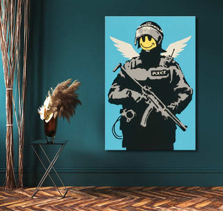 Banksy - Keep Smiling: A street pop art canvas featuring a SWAT officer with a smiley face and angel wings, complemented by dried pampas grass in a vase.