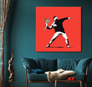 Banksy's Riot on Red canvas, featuring a flower-throwing protester, displayed in a modern living room with teal sofa and wooden side table.