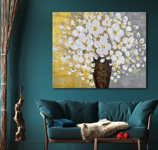 Witte Bloemen in Vaas – Dikke olieverf op canvas toont een modern bloemmotief op een rustieke achtergrond. Het schilderij hangt boven een teal bank in een stijlvolle kamer.