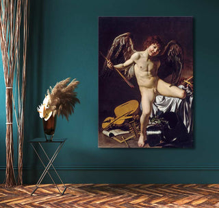 Caravaggio - Amor Vincit Omnia painting mounted on a deep teal wall, depicting a cherub with arrows amidst armor, alongside a metal table with pampas grass.