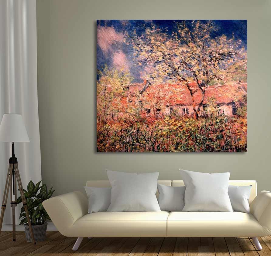 Claude Monet – Boerderij in Bloesem, een handgeschilderd olieverfschilderij met bloeiende bomen en rode daken, opgehangen boven een crèmekleurige bank in een sfeervolle woonkamer.
